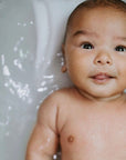 A close-up of a baby laying in a white bathtub with water around them.