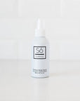 A white bottle of Só Outdoorsy Outdoor Body Spray with a white nozzle cap, standing on a white surface against a white tiled background.