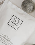 Só Clean oxygen whitening powder packaging with felt dryer balls on a neutral surface.