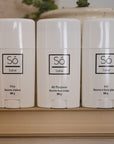 Só Luxury Collection of Salves featuring Fire warming salve Ice cooling salve and All purpose healing salve in 50 g twist-up sticks standing on a book with greenery in the background.