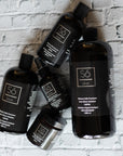 Four black bottles of various size and a black glass jar all labeled Só Silver Mission Falls Ionic Silver Solution styled on a white brick background.