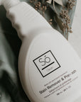 White spray bottle branded with 'Só Clean Stain Remover + Prewash' on a light marble background with green fabric and greenery.