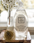 Bottle of Tangerine Dish Soap on a wooden surface with a wooden dish brush with flowers in the background