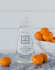 Bottle of Só Clean branded Tangerine Dish Soap with tangerines on a marble surface with a blurred light coloured background