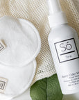 A white bottle of Só Tonic Apple Cider Vinegar facial toning spray, styled on a cream coloured mesh material white cotton rounds with a branded Só tag sewn on with a leaf in the background