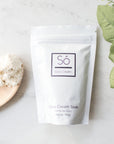 A white stand-up pouch labeled 'Só Coco Cream' and 'Coco Cream Soak' on a light marble surface, styled with a wooden spoon of white powder and green leaves.