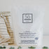 A package of Só Clean Oxygen Whitening Powder with a small scoop and a cloth beside it, on a white background with eucalyptus leaves.