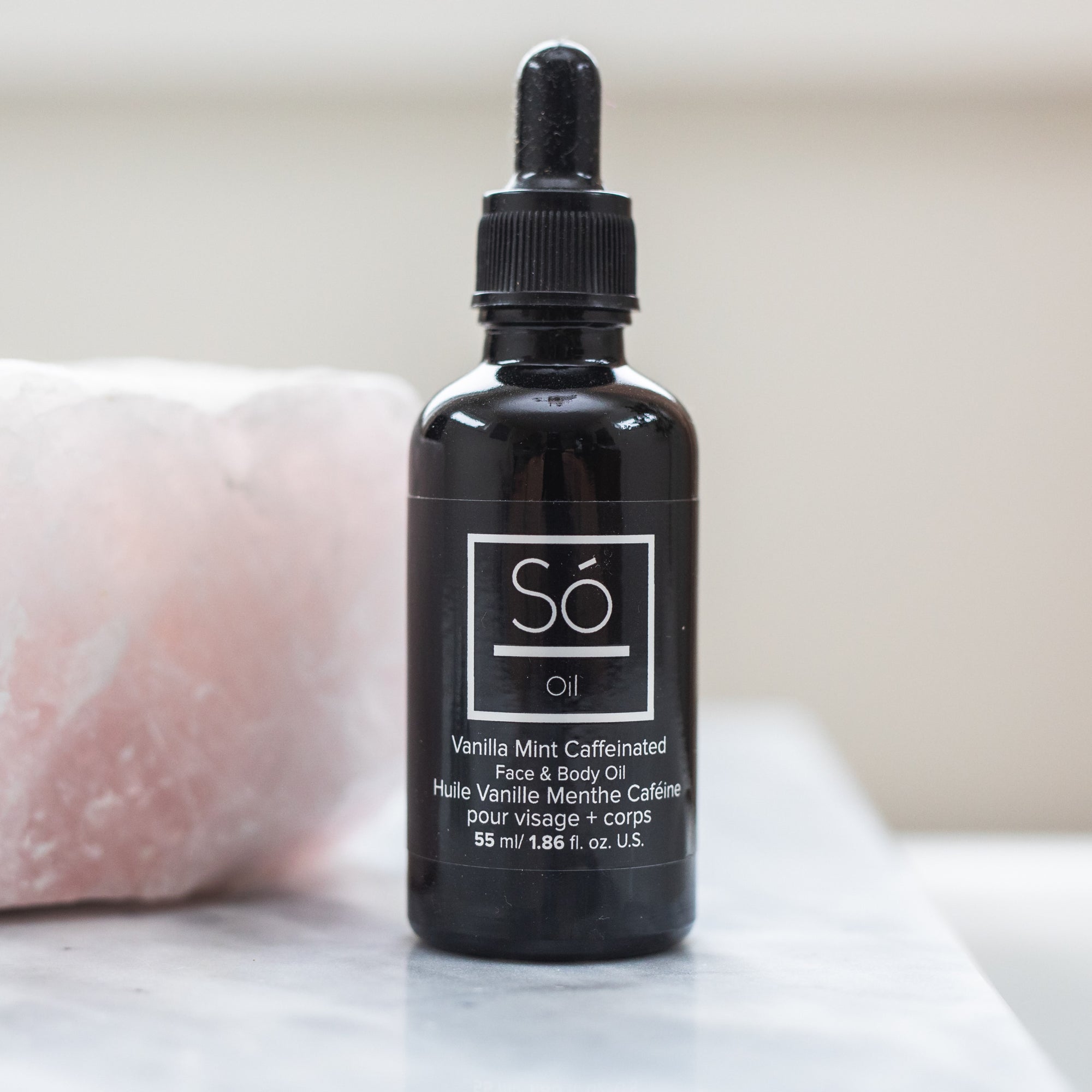 A black bottle labelled "So Oil Vanilla Mint Caffeinated" on a counter with a pink quartz stone