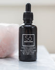 A black bottle labelled "So Oil Vanilla Mint Caffeinated" on a counter with a pink quartz stone