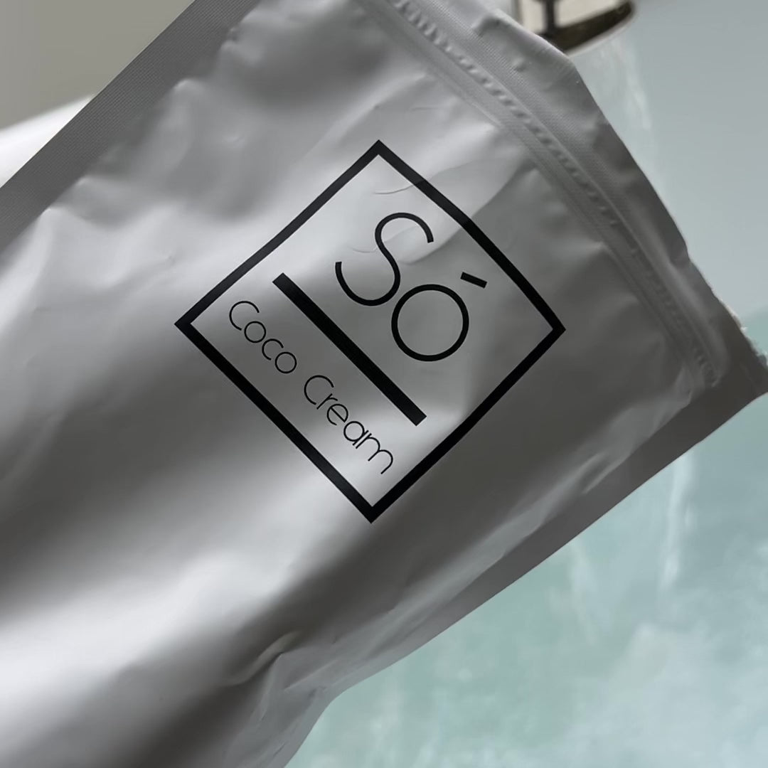 Video showing a Só Coco Cream bath soak being poured into a bath with running water and swirling water showing the product