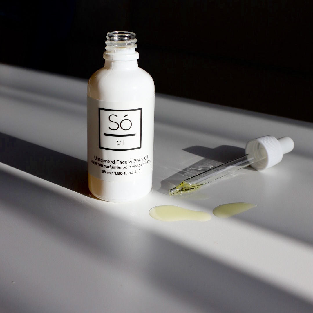 A white bottle with a dropper containing unscented oil, placed on a surface with a few drops of oil visible in front of the bottle.