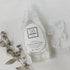 A clear bottle of Só Clean Tangerine Dish Soap with a white label, surrounded by some plant leaves and clear rocks on a white background.
